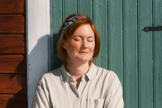 Person som står mot ladugårds vägg och njuter av vårsolen