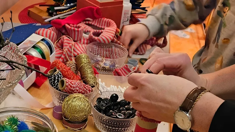 Bilden är ett foto på ett bord fullt av material till att pyssla, med två par händer som limmar och dekorerar.