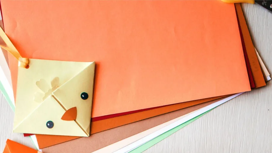 Bilden är ett fotografi av färgade pappersark och ett bokmärke som föreställer en kyckling.