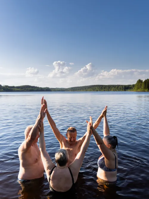 Fyra personer som står i ring i vattnet med händerna i luften