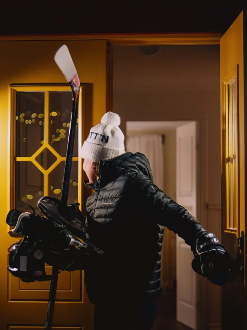 Ungdom på väg ut från ytterdörren men hockeyklubba i handen