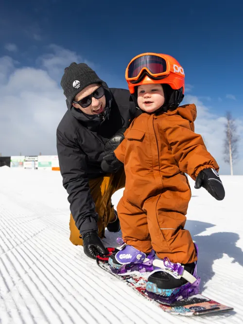Person som hjälper sitt barn att åka snowboard