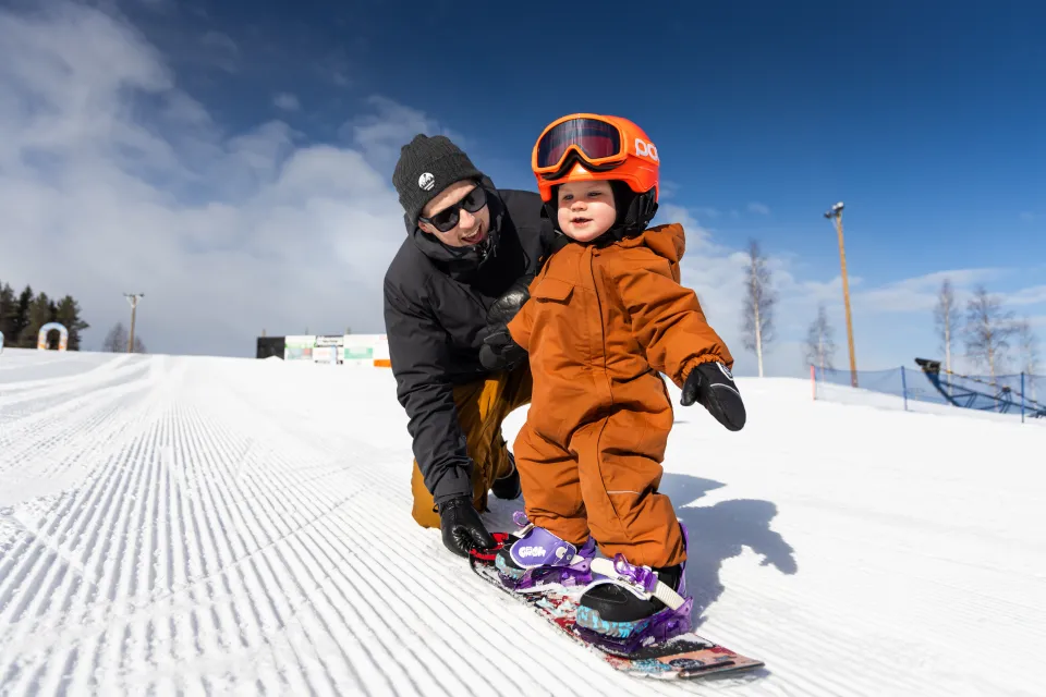 Person som hjälper sitt barn att åka snowboard