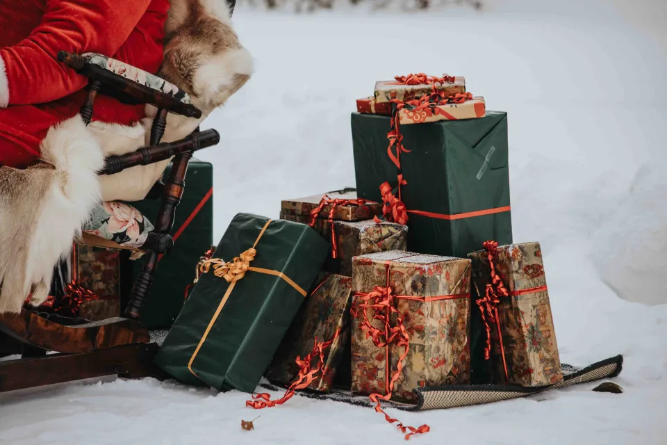 Hög med julklappar ligger i snön brevid tomte